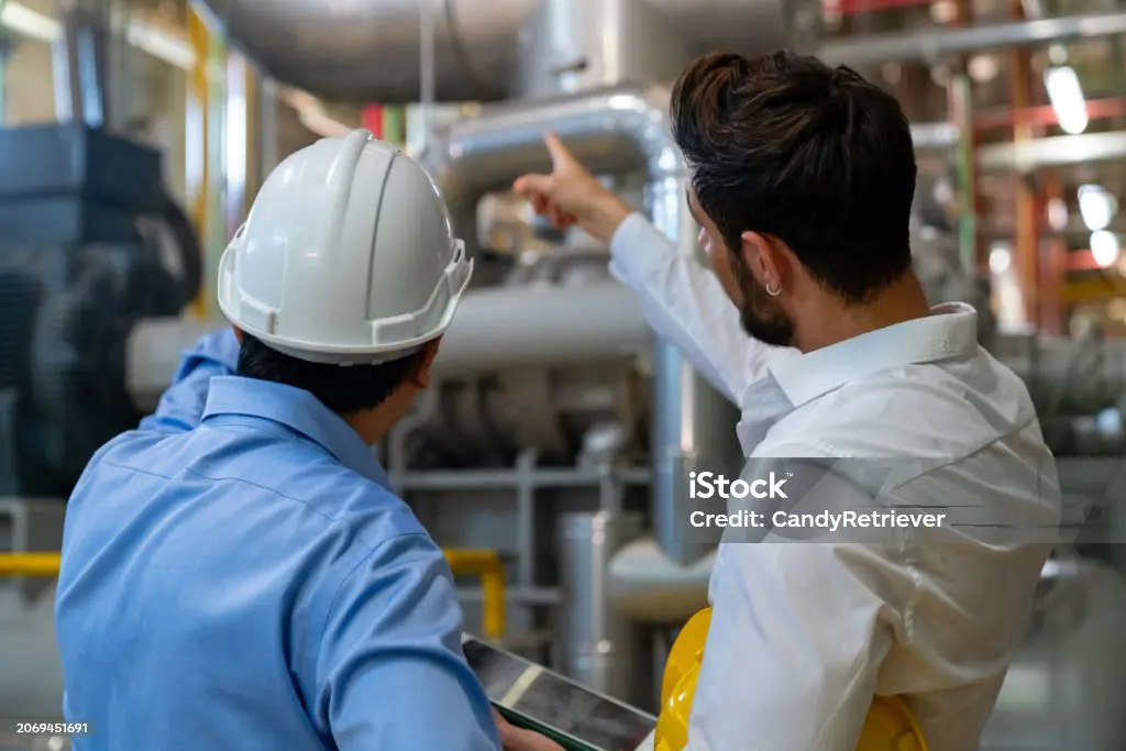 Two engineers inspecting industrial piping in a factory.